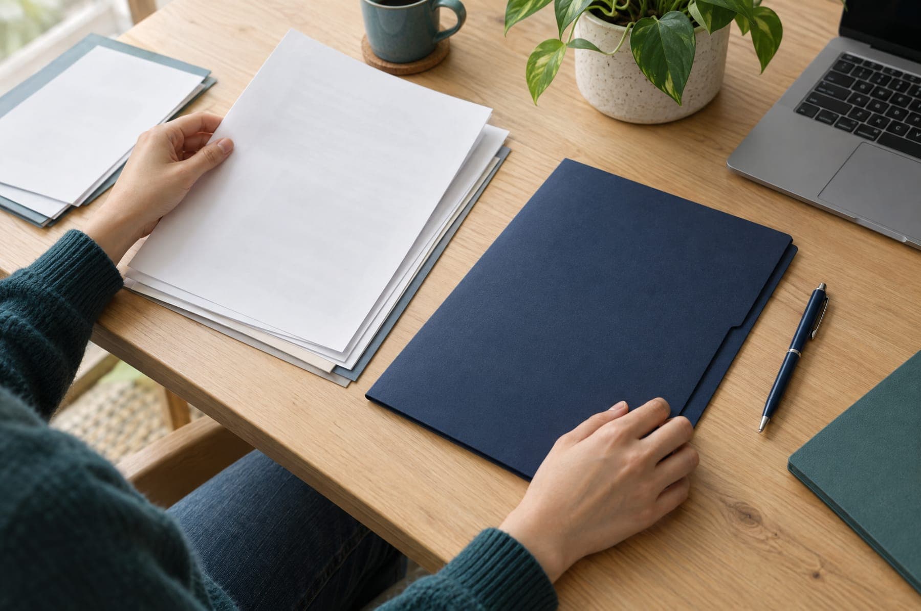 Hands organising academic papers in a navy folder on a wooden desk